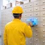 A brass cabinet of hundreds of drawers with exactly one open and glowing blue inside